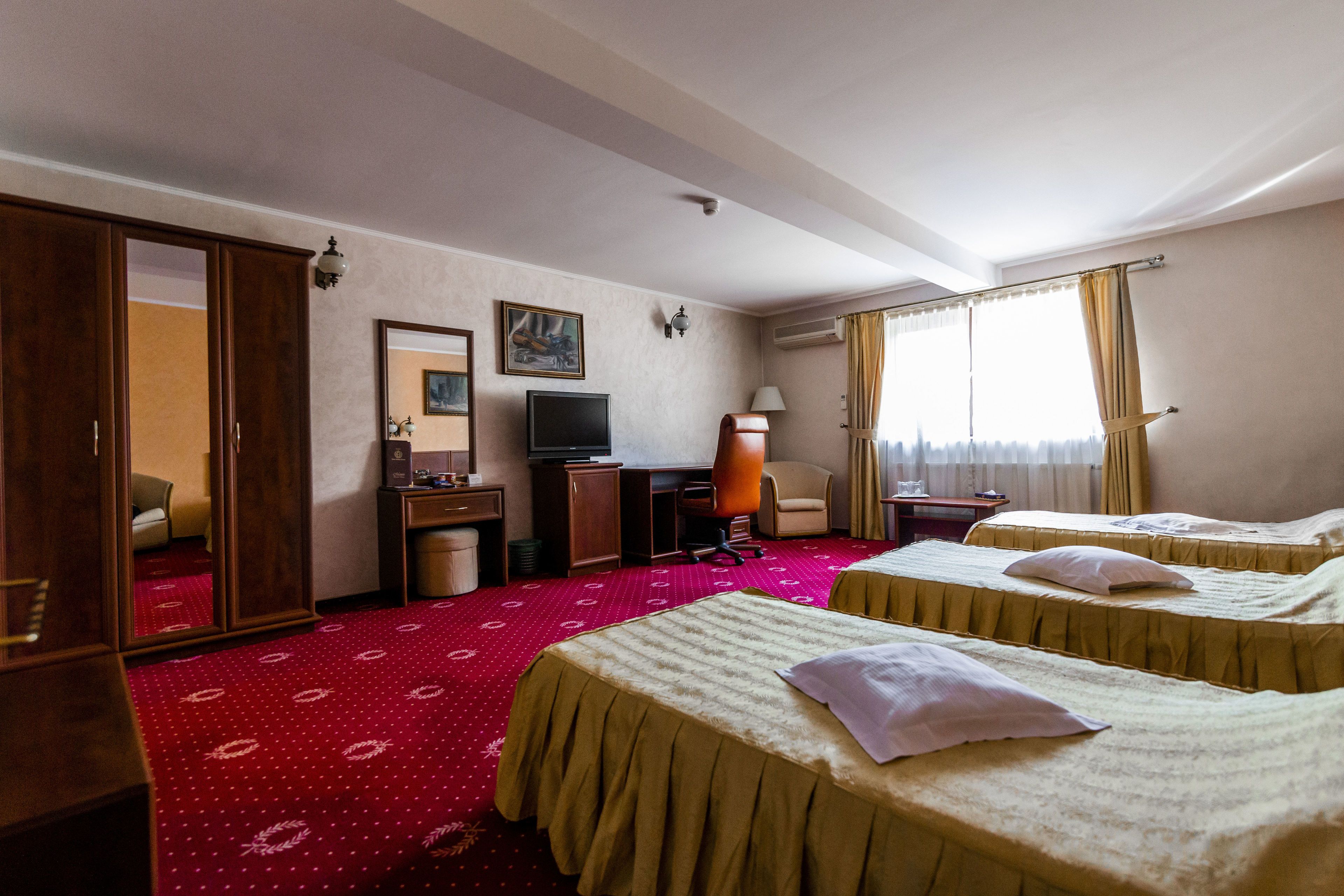 Una camera d'albergo con due letti, una scrivania, una televisione, una sedia e un armadio.