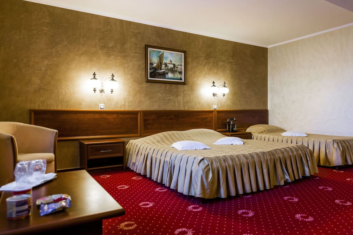 Habitación de hotel con dos camas, cabecero de madera, alfombra roja e iluminación en la pared.