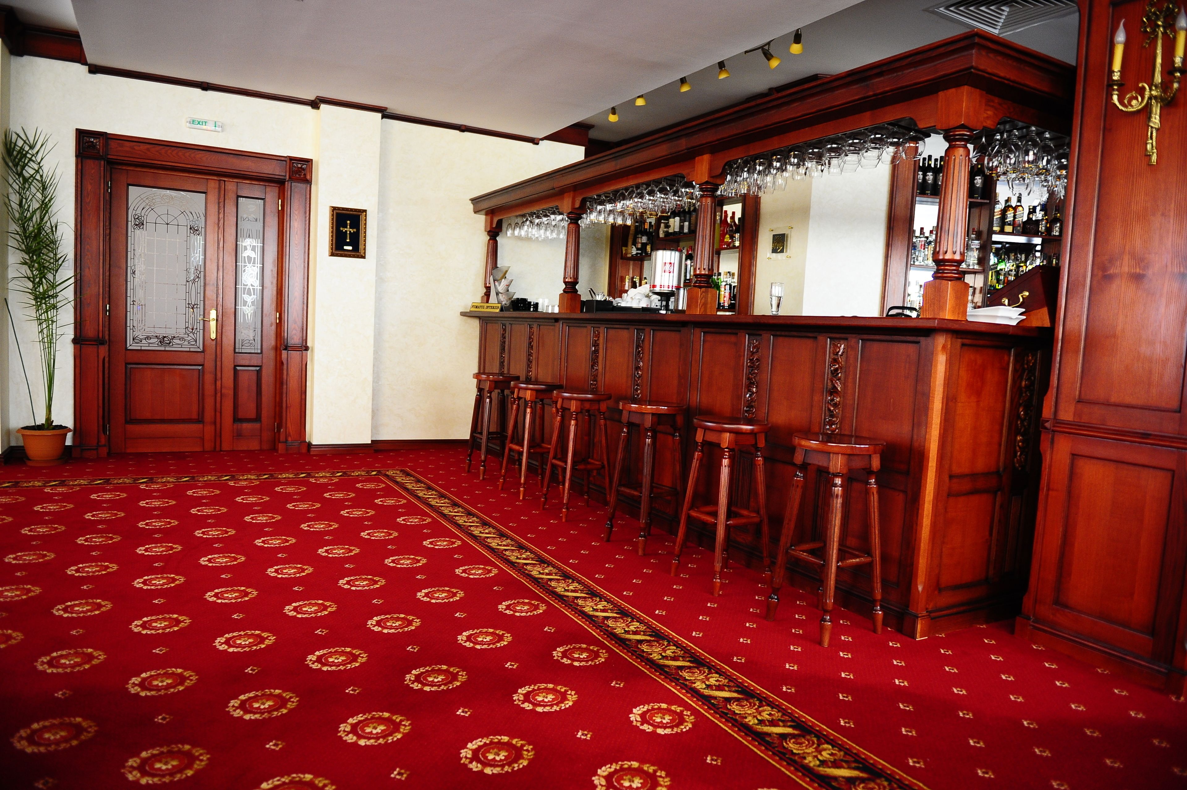 Zona de bar con taburetes de madera, alfombra roja y un espejo que refleja la barra.
