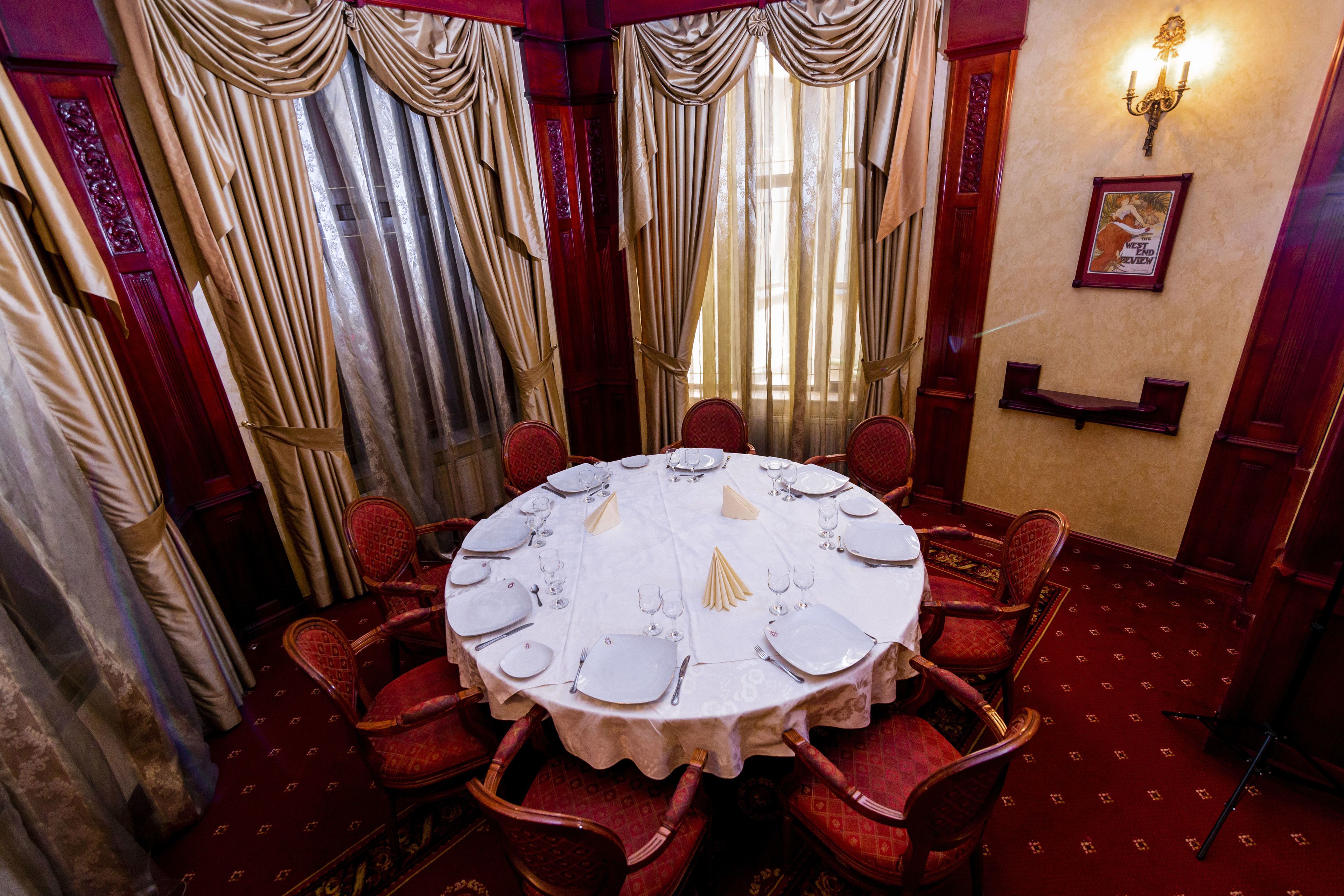A dining room with a round table set for six, surrounded by red upholstered chairs.
