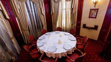 A dining room with a round table set for six, surrounded by red upholstered chairs.