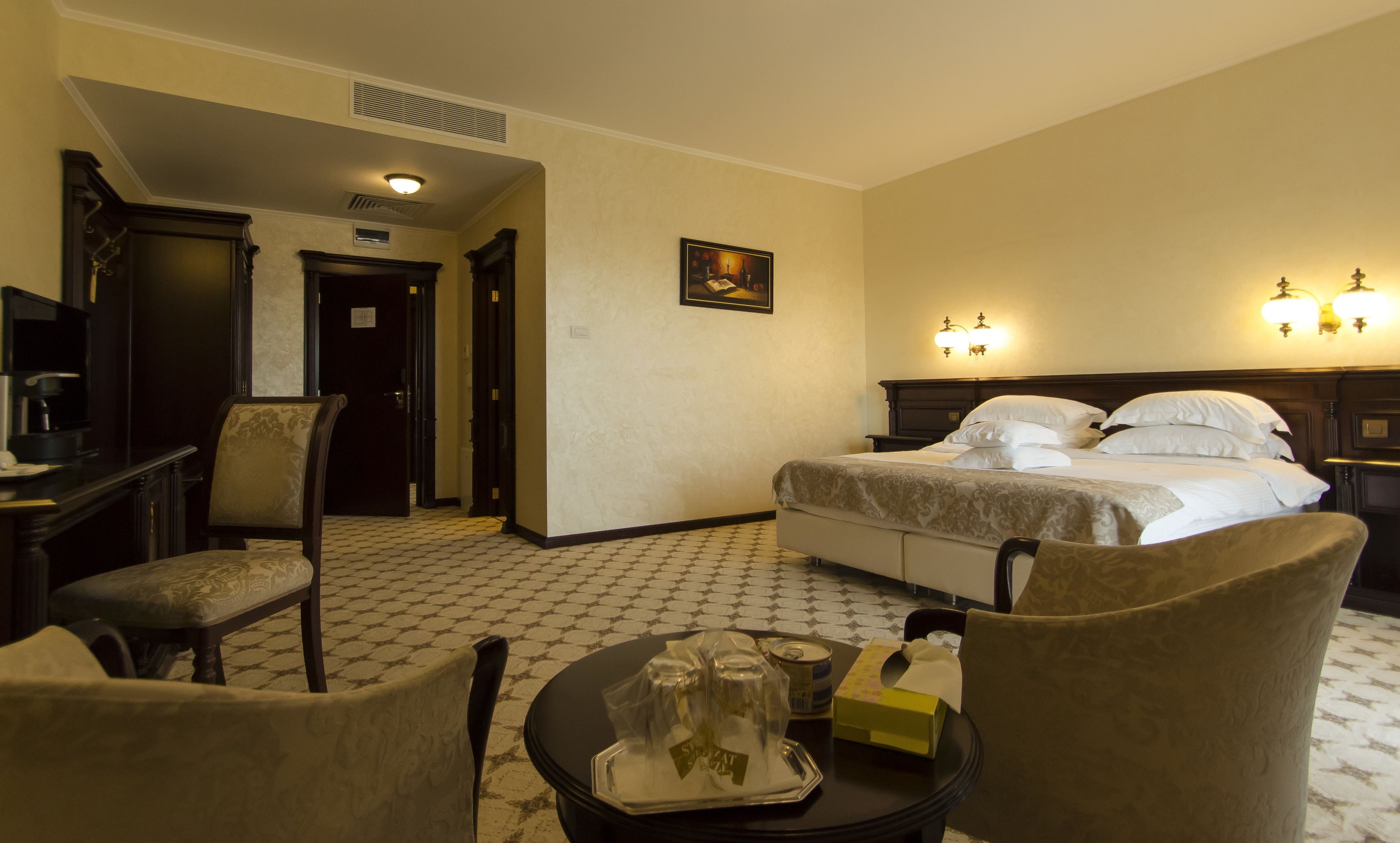 Una camera d'albergo con un letto, una scrivania con una sedia, un tavolino con vassoio e un quadro appeso al muro.
