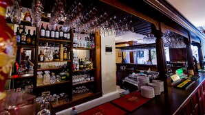 A bar area with shelves of liquor bottles, glasses, and a bar counter with stacked plates. - Hotel Golden House (Craiova)