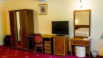 Ein Hotelzimmer mit einem Holztisch, einem Fernseher, einem Kleiderschrank, einem Sessel und einem Bett mit gemustertem Überwurf.