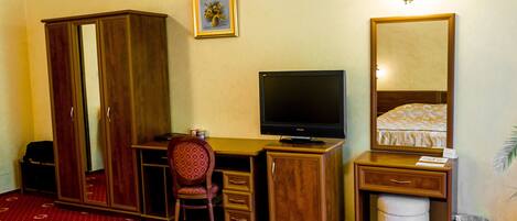 A hotel room with a wooden desk, a television, a wardrobe, a chair, and a bed with a patterned bedspread.