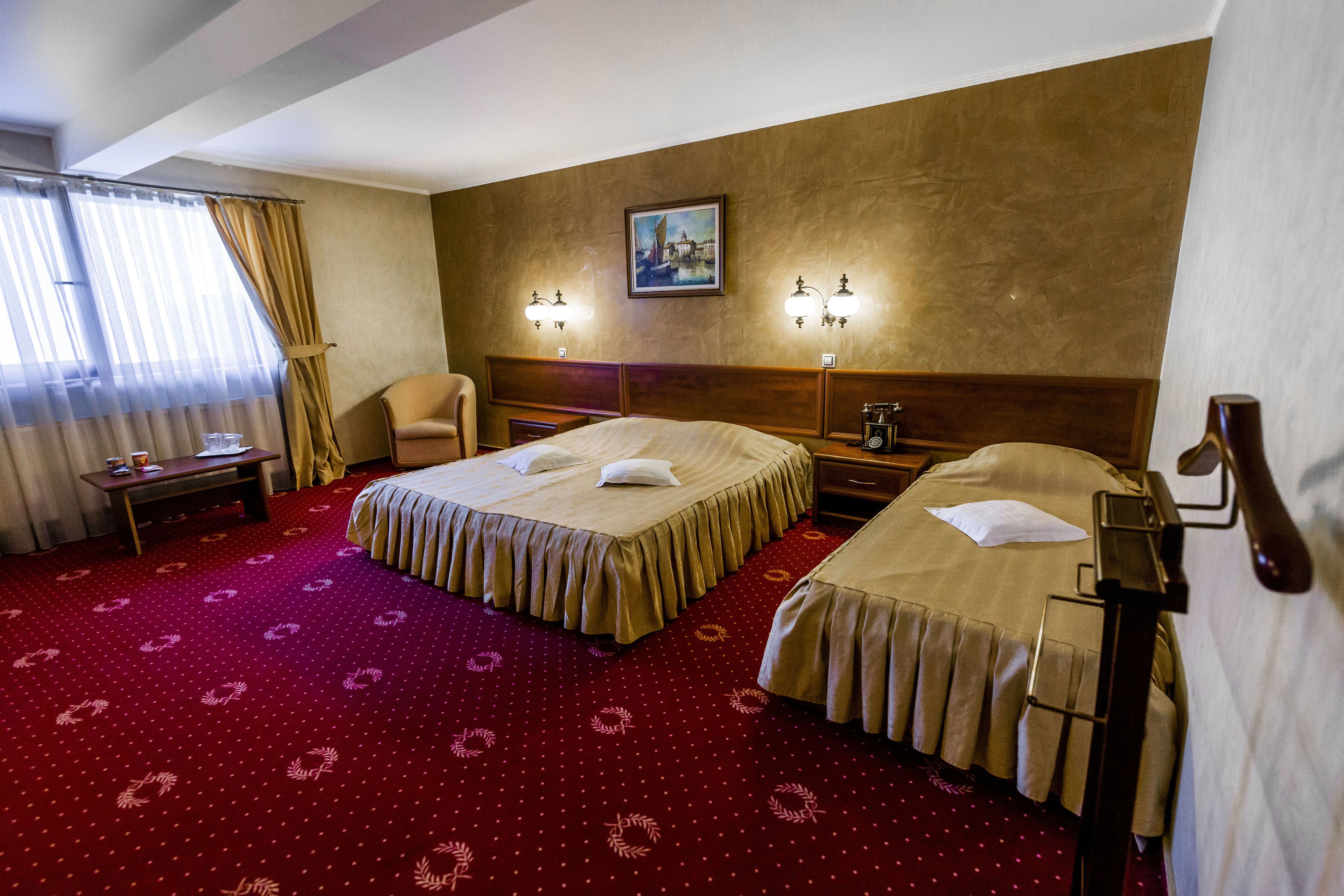 A hotel room with two beds, a desk, a chair, and a painting on the wall.