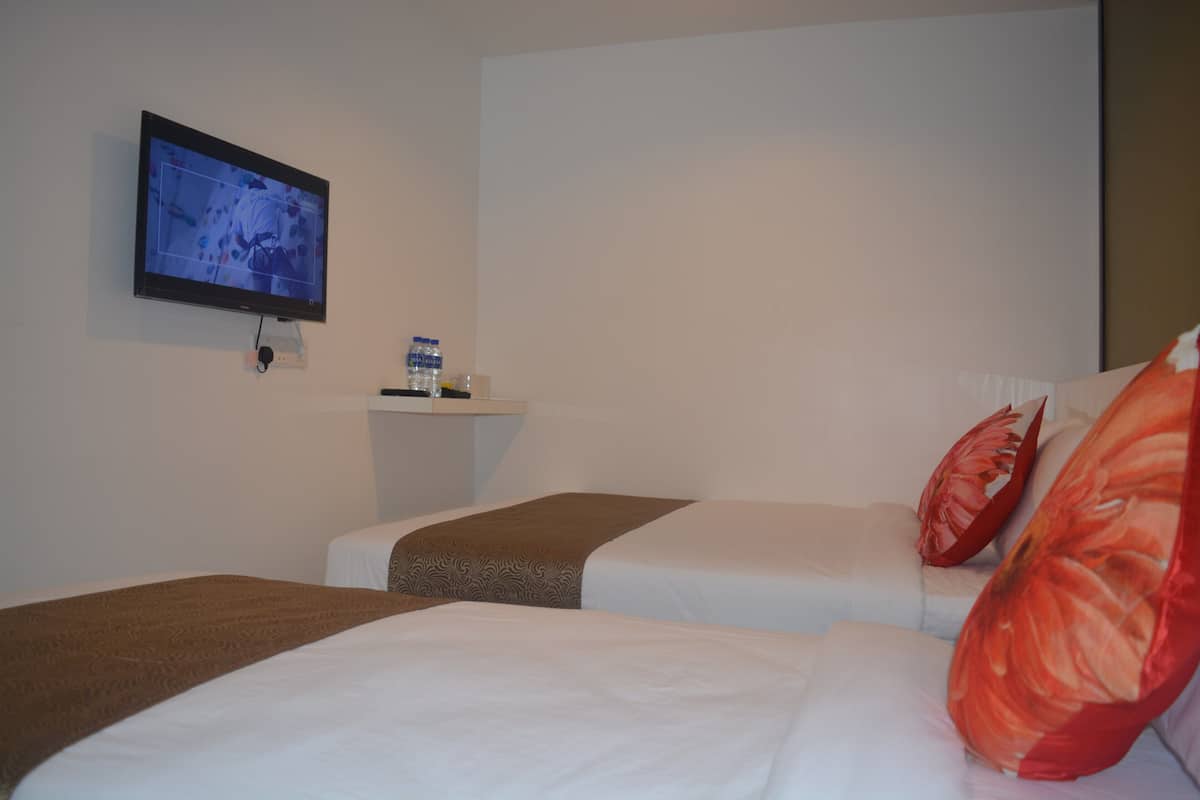 Une chambre d’hôtel avec deux lits, un téléviseur fixé au mur et une petite table avec une bouteille d’eau.