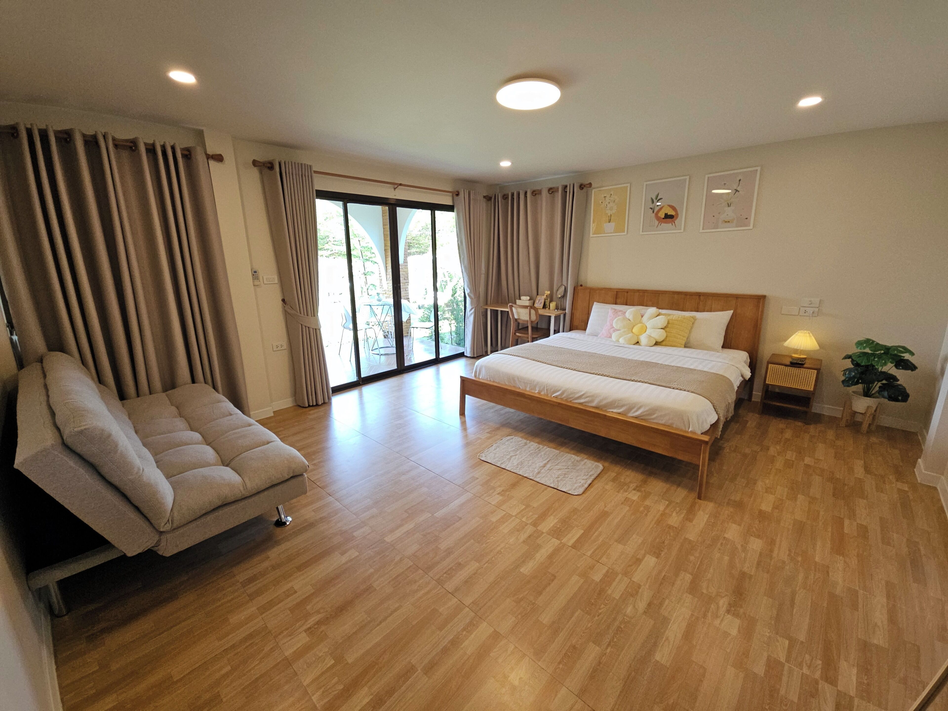 A spacious bedroom with a large bed, a sofa, a desk, and a view of the outdoors.