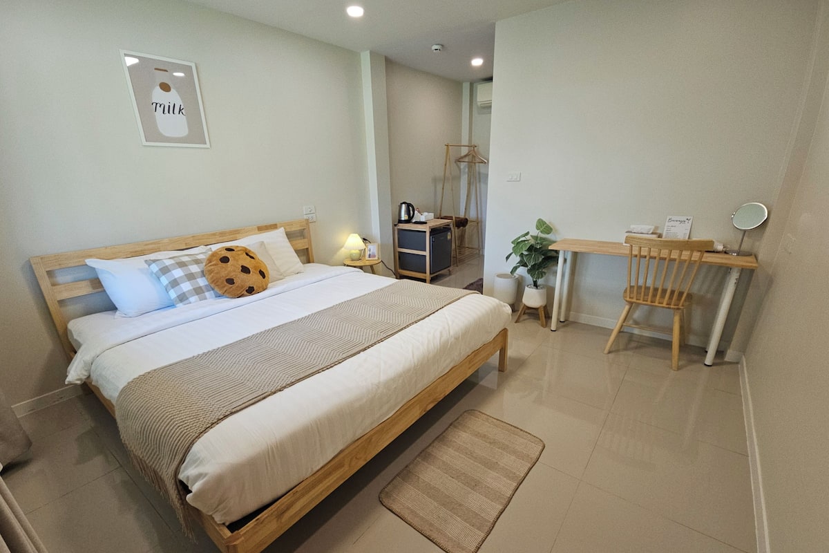 A bedroom with a wooden bed, a desk, and a chair. There is a small table with a plant and a sign.