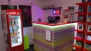 A hotel reception area with a Coca-Cola refrigerator, a neon 'Café' sign, and a photo display wall. - Hostel Lumiere (Milan)