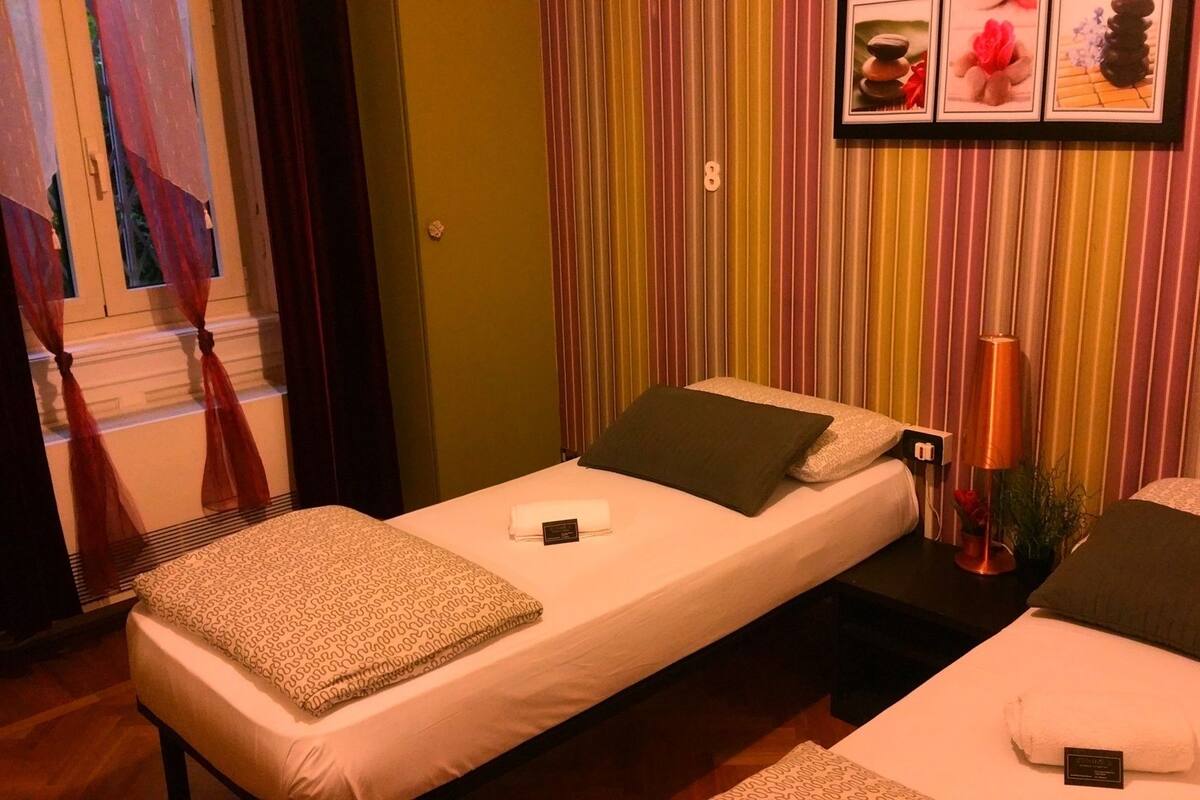A single bed with a pillow and a blanket, a bedside table with a lamp, and a wall with vertical stripes.