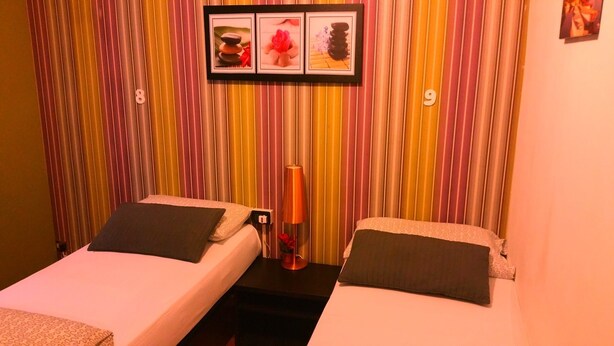 A room with two beds, striped curtains, a framed picture above the beds, and a small table with a lamp between them. - Hostel Lumiere (Milan)