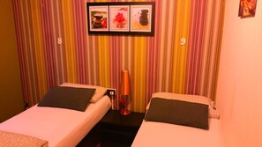 A room with two beds, striped curtains, a framed picture above the beds, and a small table with a lamp between them. - Hostel Lumiere (Milan)