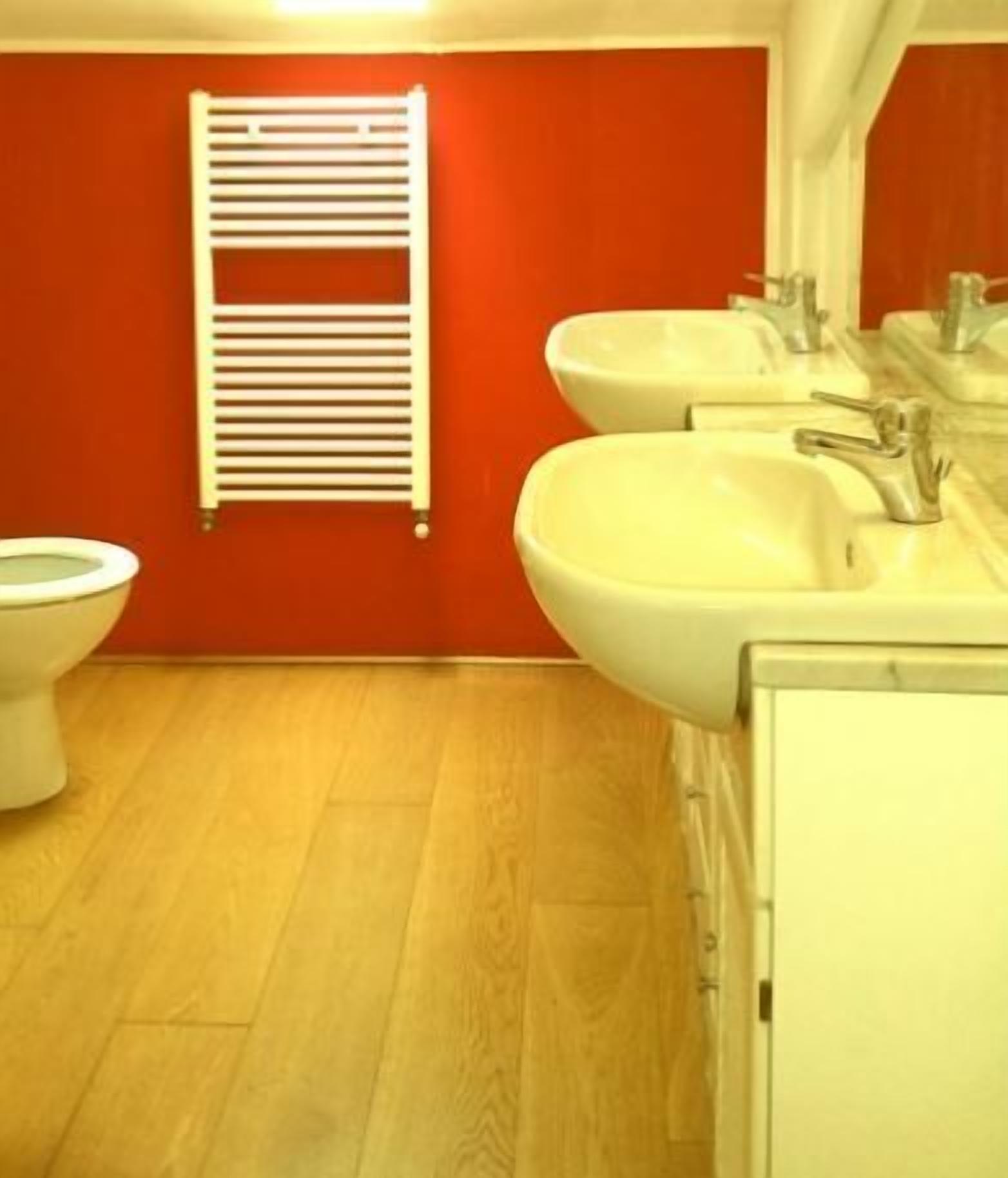 Un baño con inodoro, dos lavamanos y un perchero para toallas.