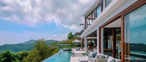 A modern outdoor pool area with a view of the mountains, a covered seating area, and a glass-enclosed room.