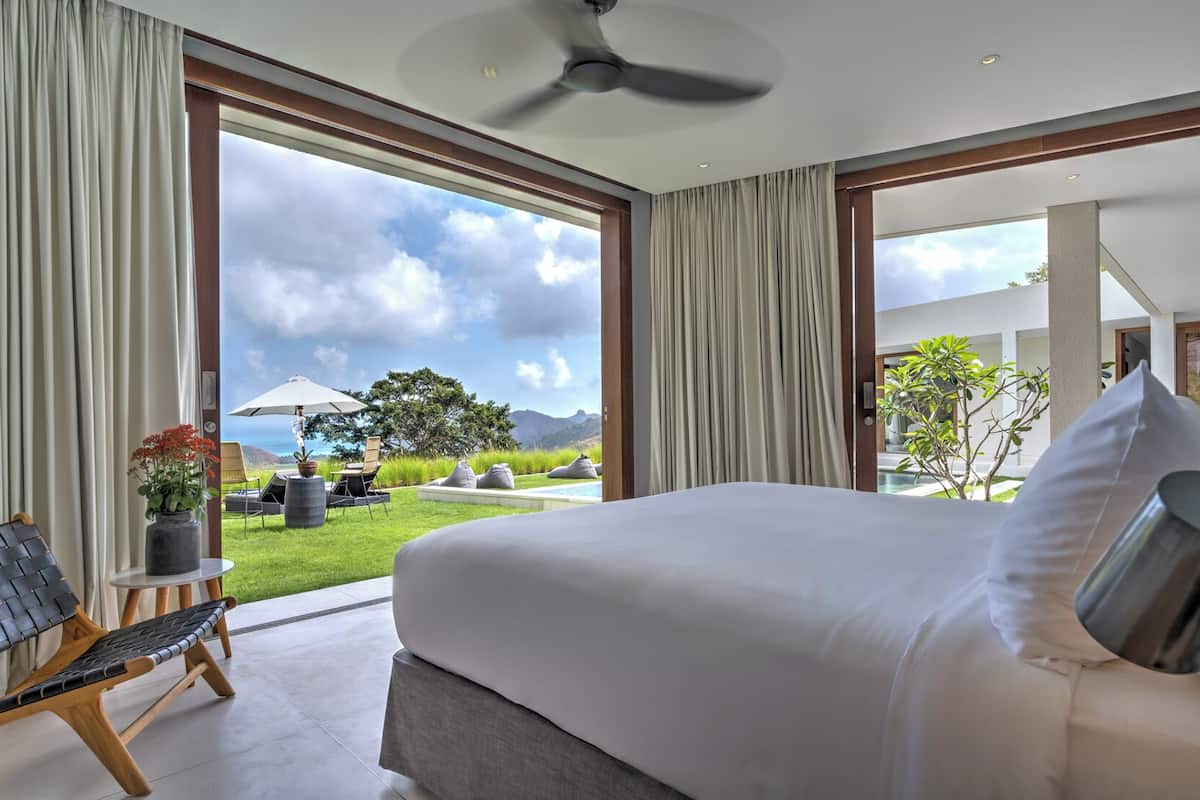 Un dormitorio con una cama grande, una silla, una mesita con una planta y vistas a una piscina y jardín.