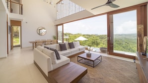 Un salón amplio con un gran ventanal, un ventilador de techo y un comedor con vistas al exterior.