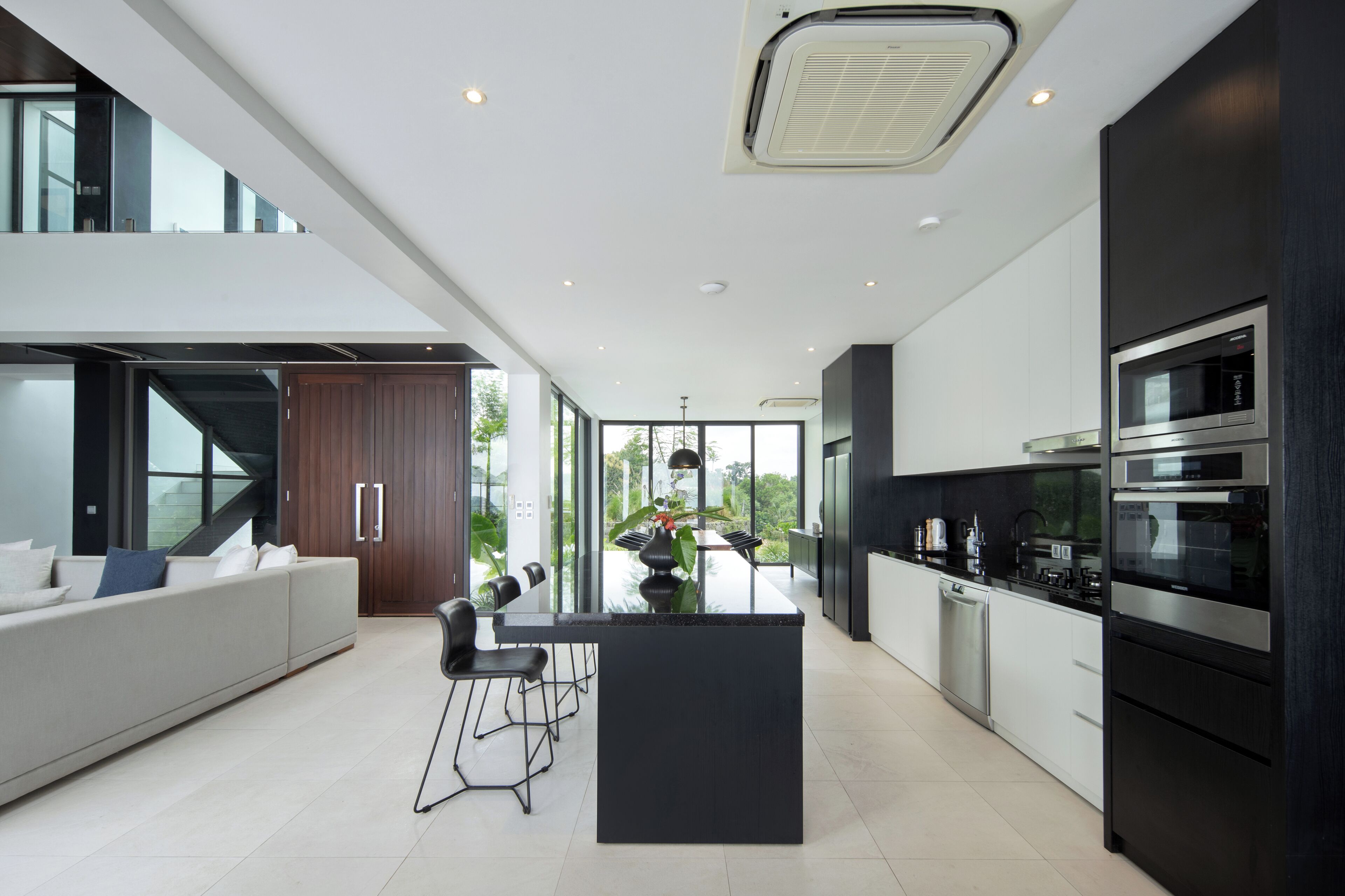 A modern kitchen with a central island, built-in appliances, and a large window overlooking greenery.