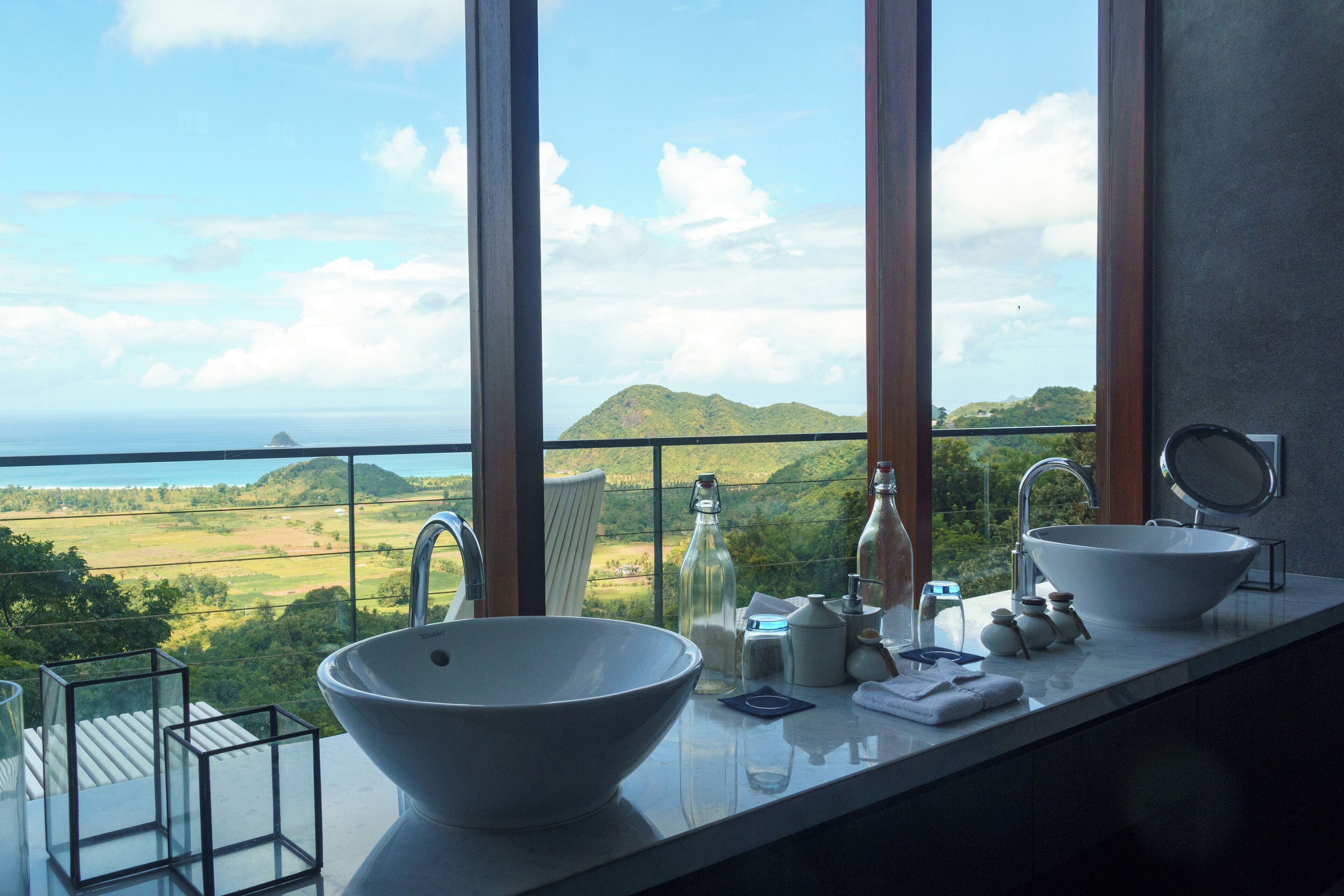 A bathroom with a large bowl sink, a mirror, and a view of a green landscape through large windows.