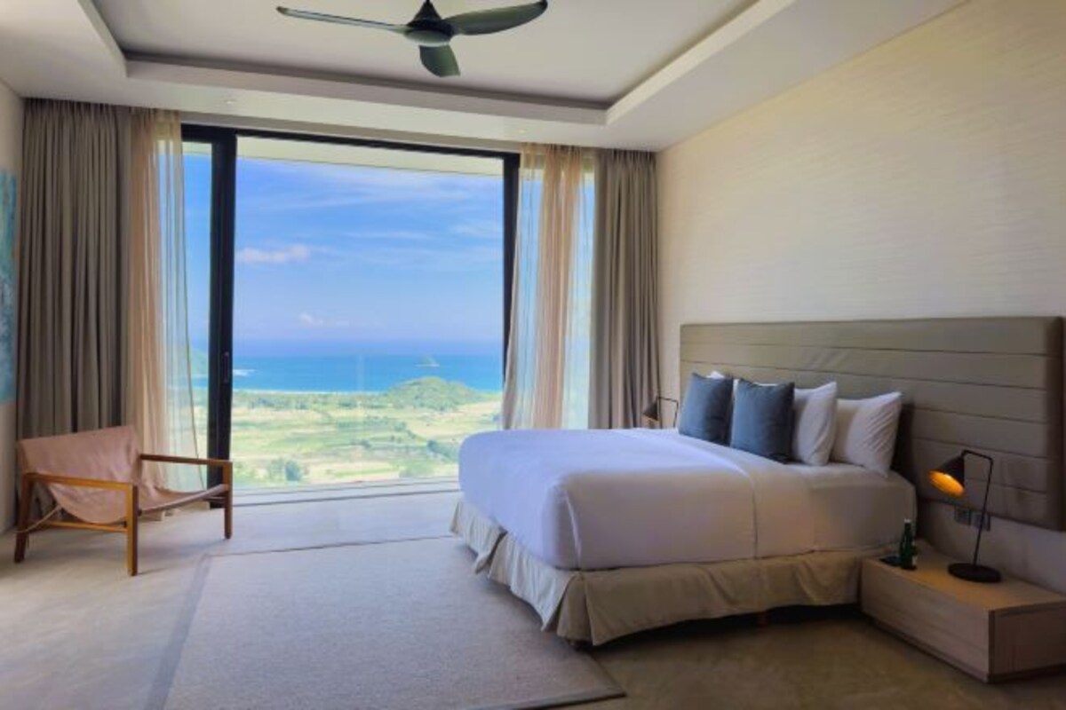 Habitación de hotel con una cama grande, una silla, una mesita de noche y vistas al océano.