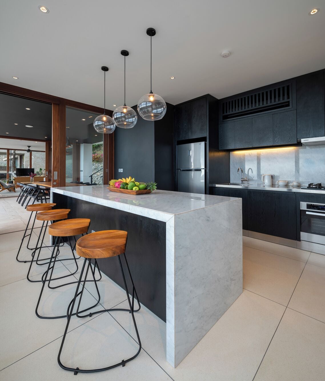 Una cocina moderna con una isla central, taburetes de bar, electrodomésticos de acero inoxidable e iluminación colgante.