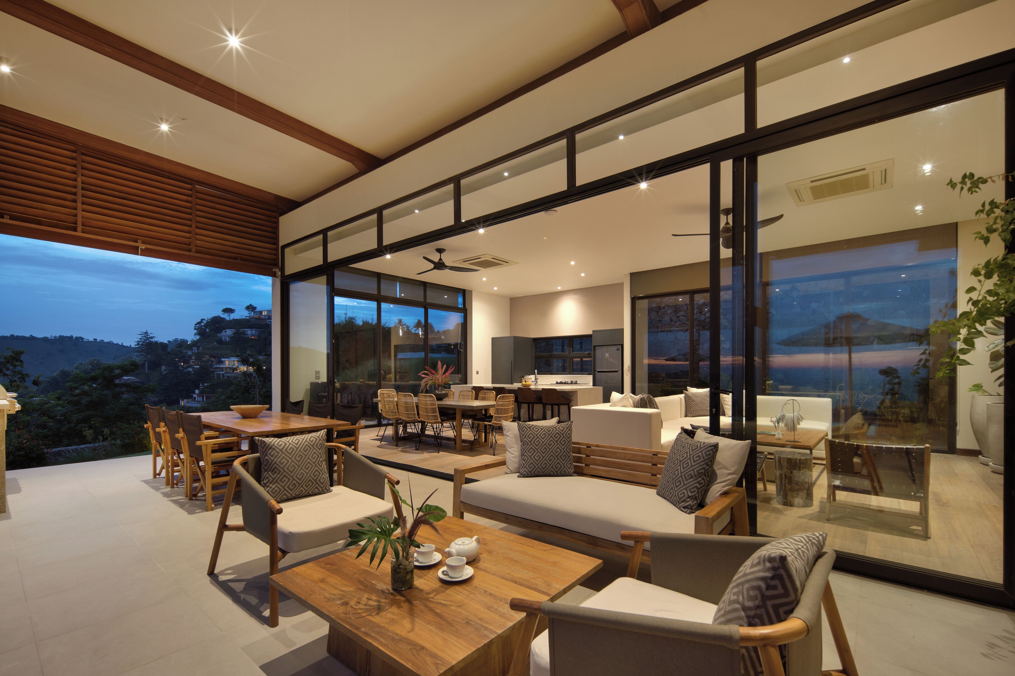 Amplia sala de estar con un gran muro de vidrio, muebles de madera y vistas al exterior.