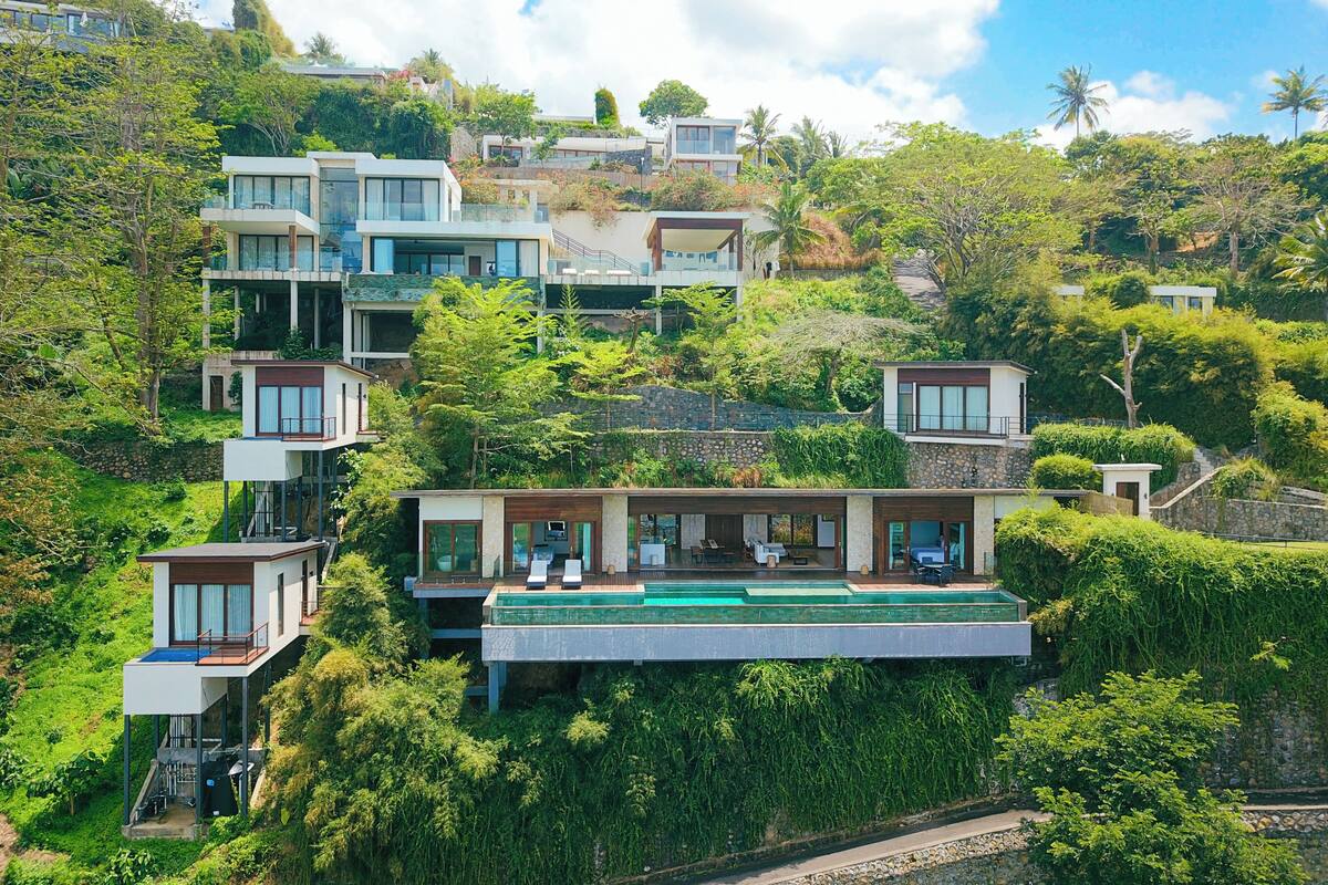 Un moderno barrio residencial en la ladera con varias casas que tienen balcones, ventanas amplias y abundante vegetación.