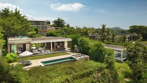Una casa moderna con piscina, mobiliario exterior y abundante vegetación.