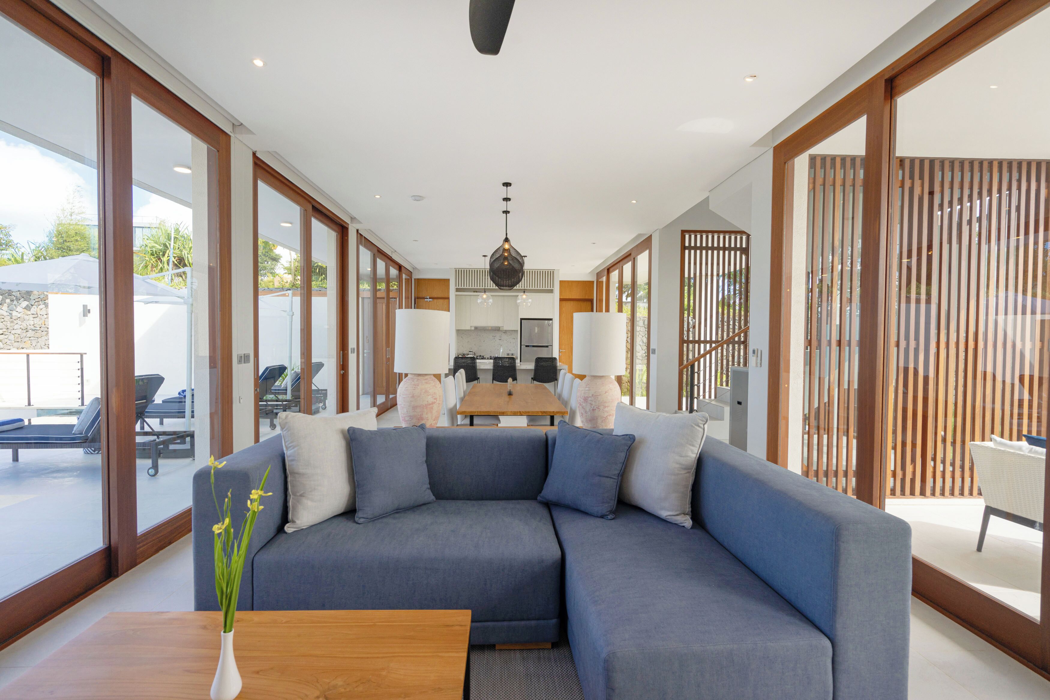 Een moderne woonkamer met een modulaire bank, een houten salontafel, en een eethoek met een keuken op de achtergrond.