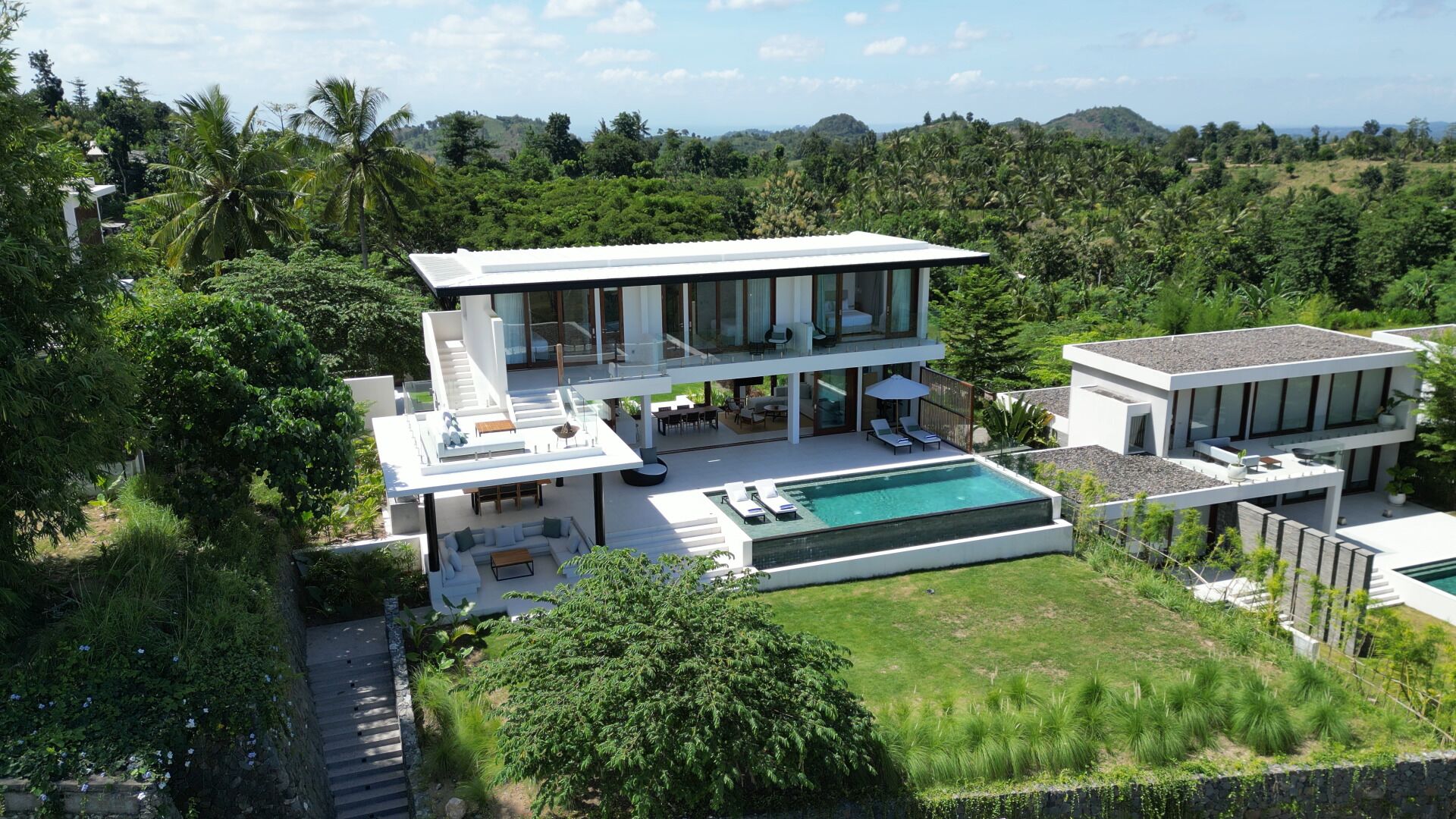 A modern two-story house with a pool, surrounded by lush greenery and hills.