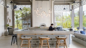 Cocina moderna con una isla central, taburetes de bar, lámparas colgantes y una persona trabajando en la barra.