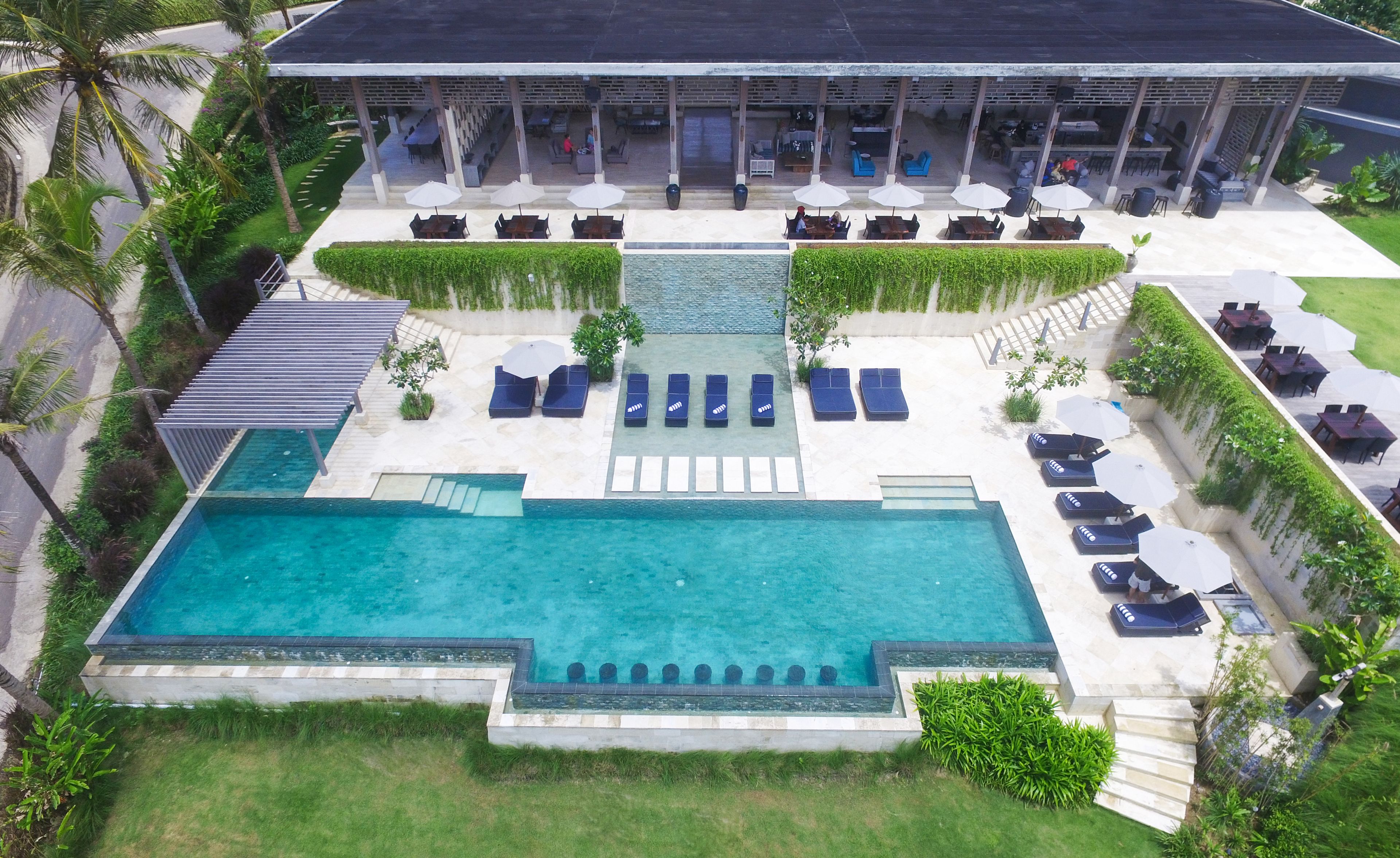 A rooftop pool area with lounge chairs and umbrellas, surrounded by greenery and a covered seating area.