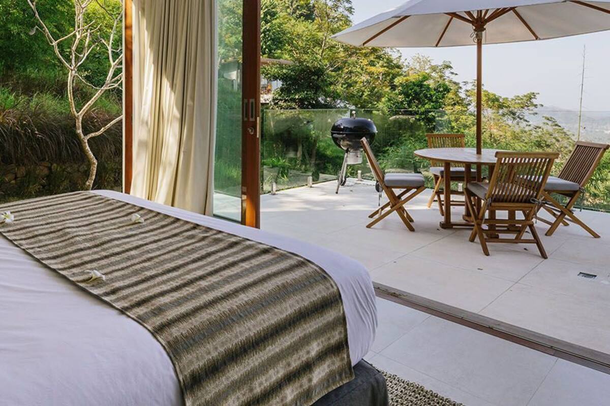 Un dormitorio con una cama grande, vistas al exterior y un patio con mesa y sillas.