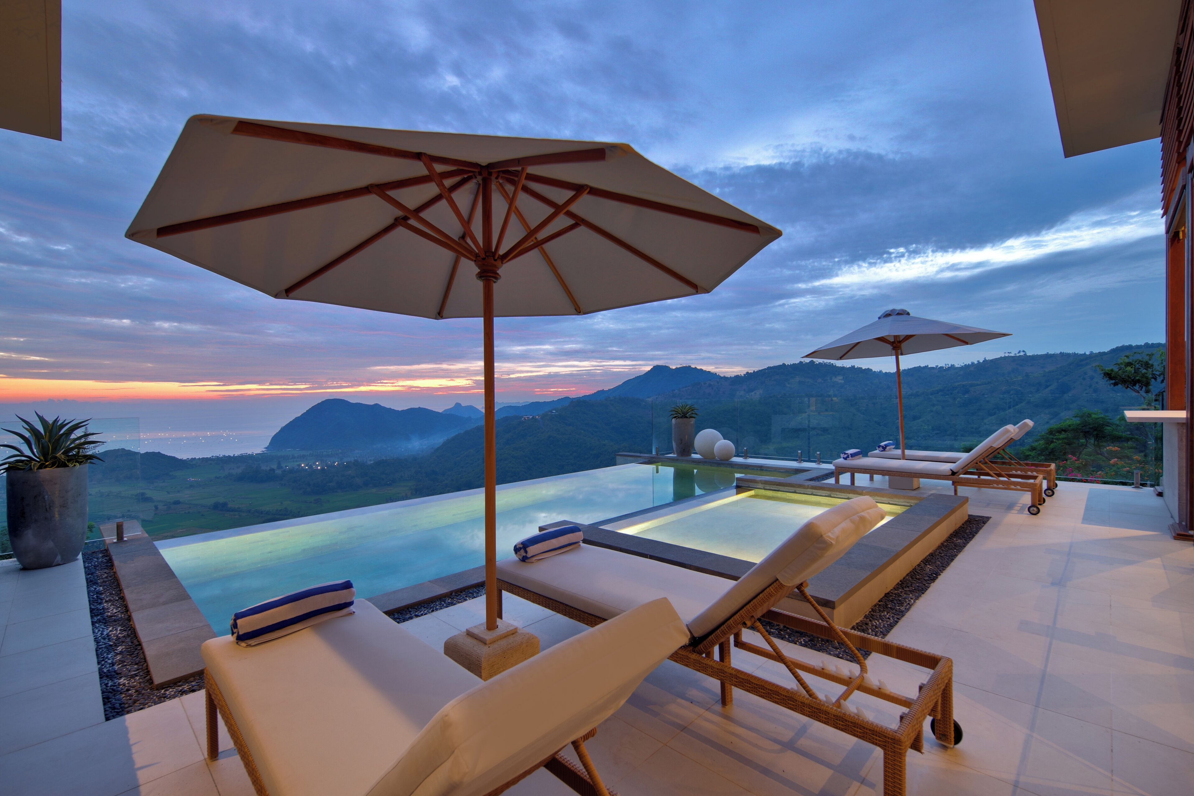 A poolside area with lounge chairs, umbrellas, and a view of the mountains.