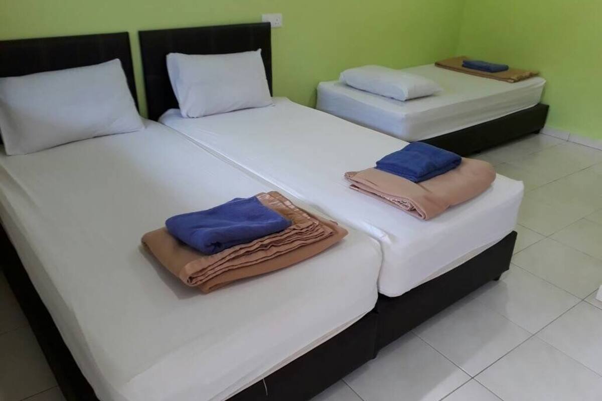 A hotel room with two beds, each with white linens and pillows, and a small table with a blue towel.