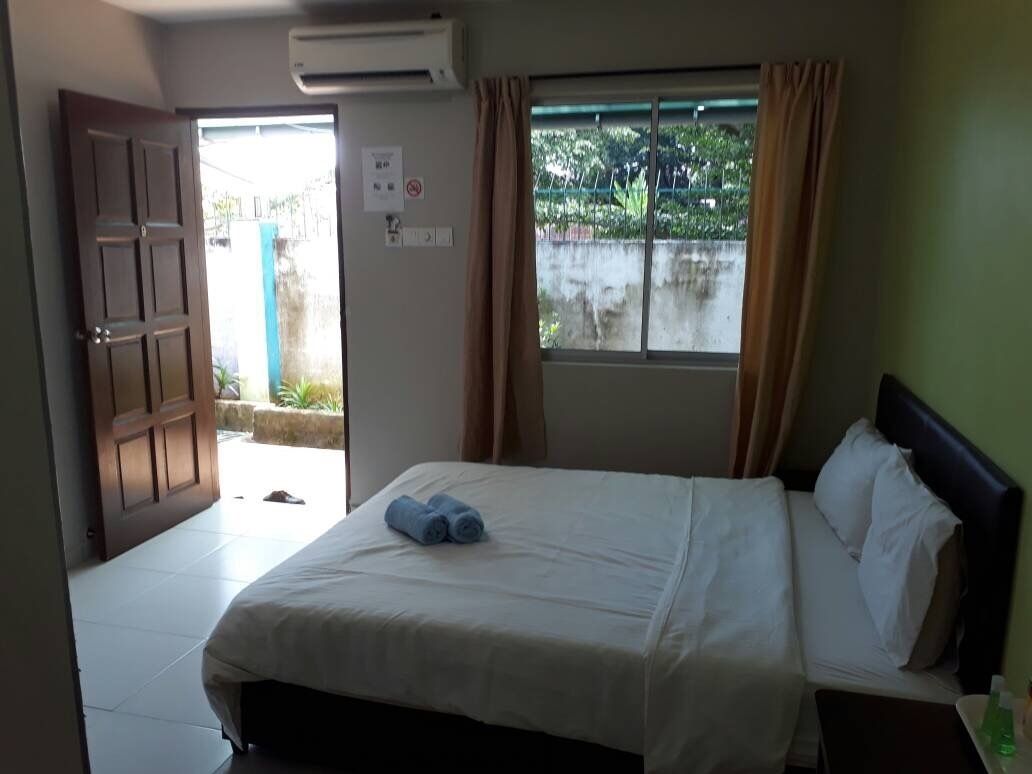 A hotel room with a bed, a window with curtains, a door, and an air conditioning unit.