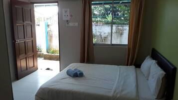 A hotel room with a bed, a window with curtains, a door, and an air conditioning unit.