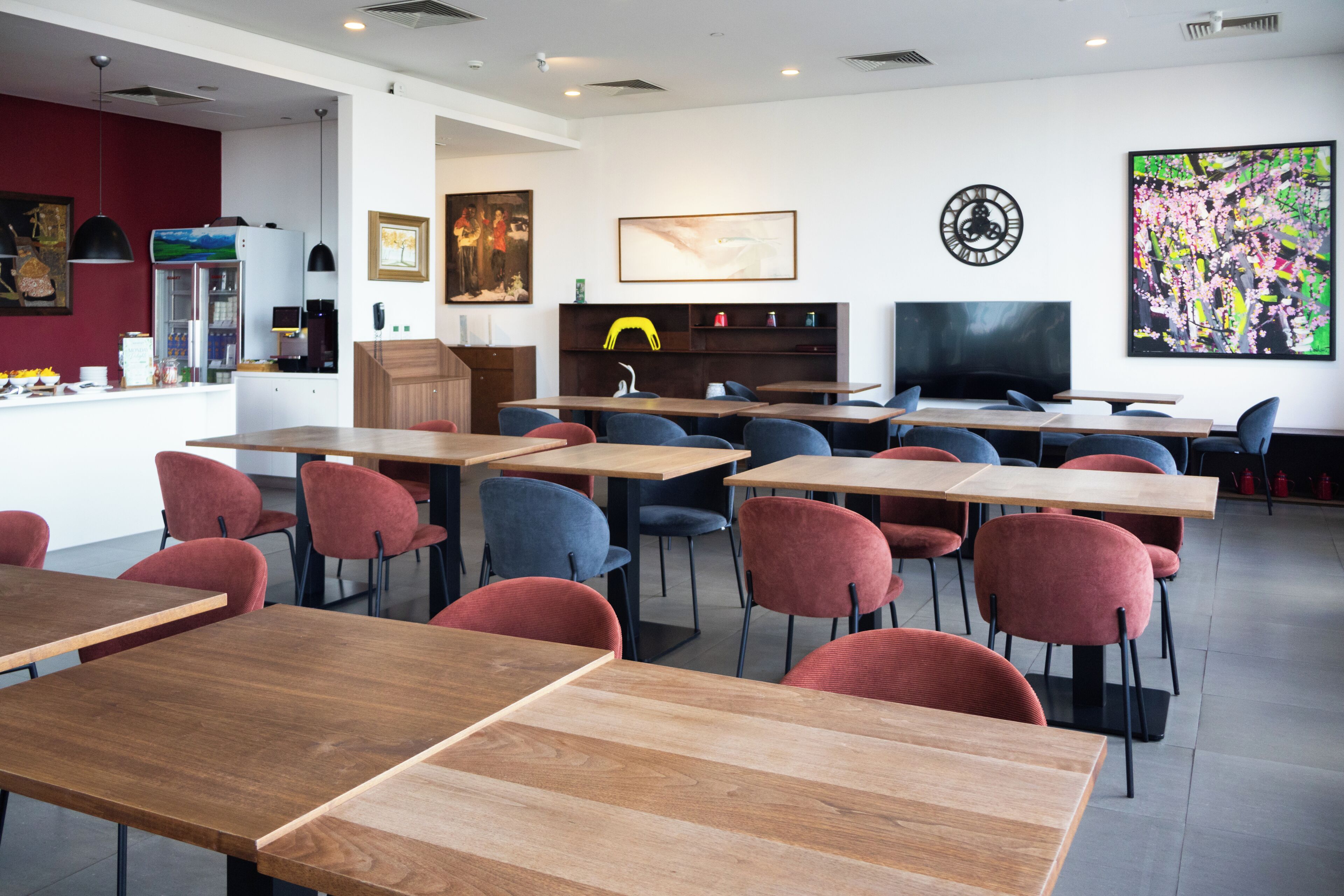 A modern dining area with wooden tables and chairs, a television, and artwork on the walls.