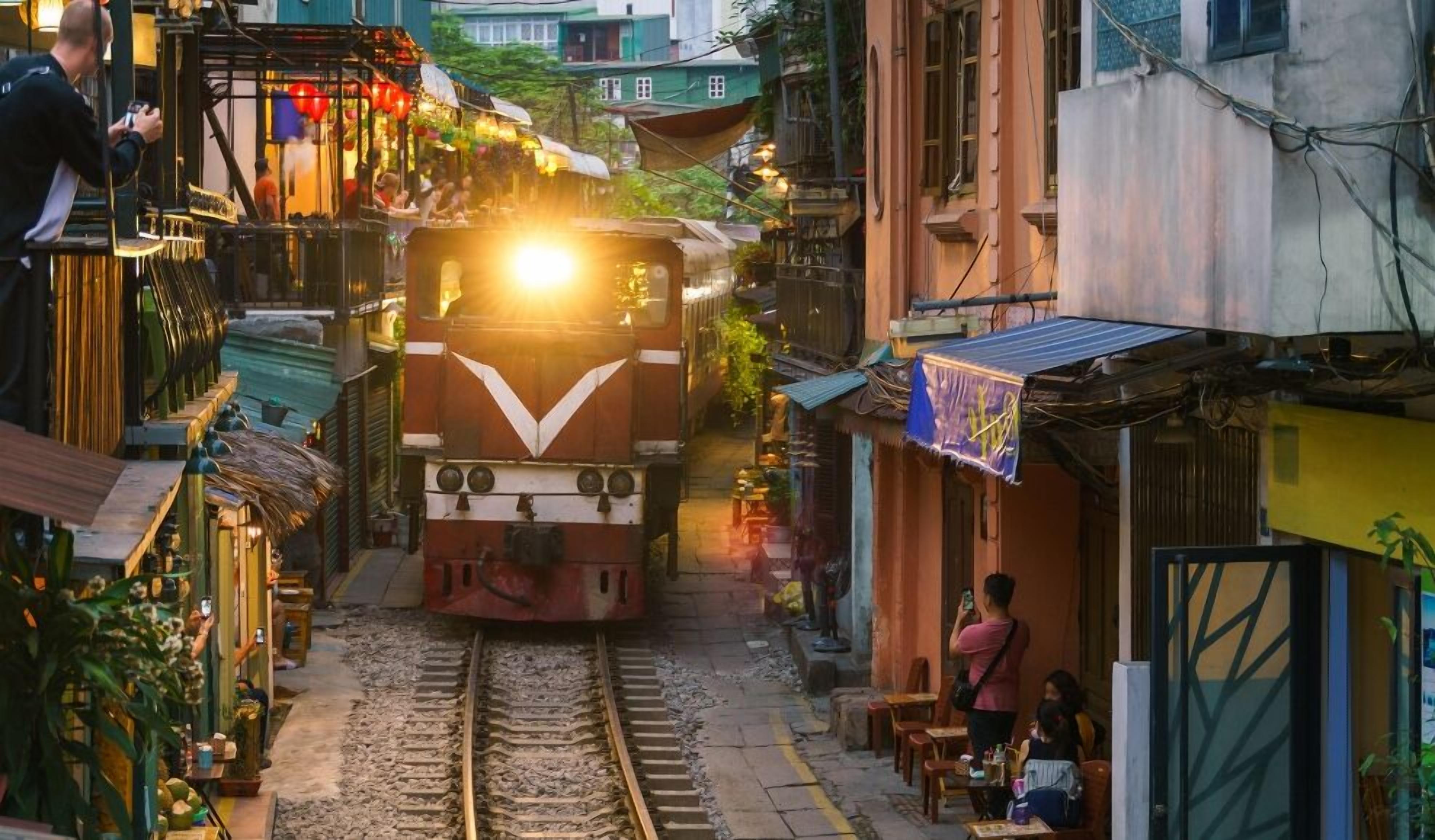 A train moving through a narrow urban street flanked by buildings and small shops.