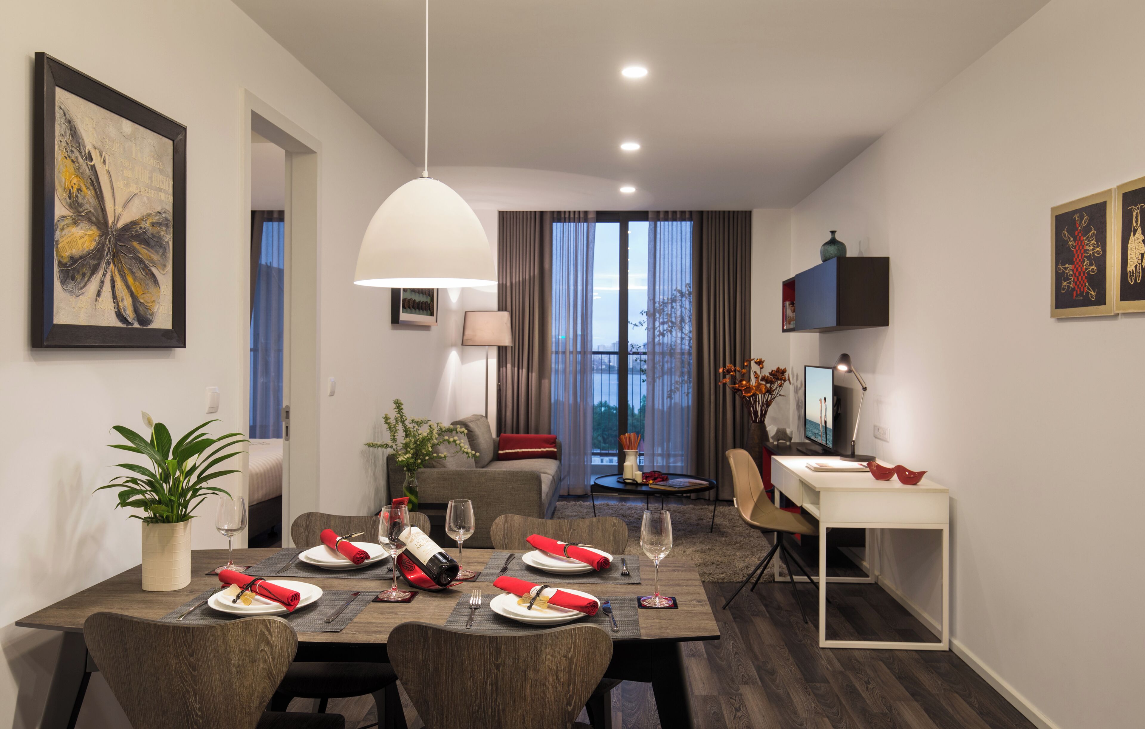 A modern hotel room with a dining area, a sofa, a TV, and a balcony with a view.