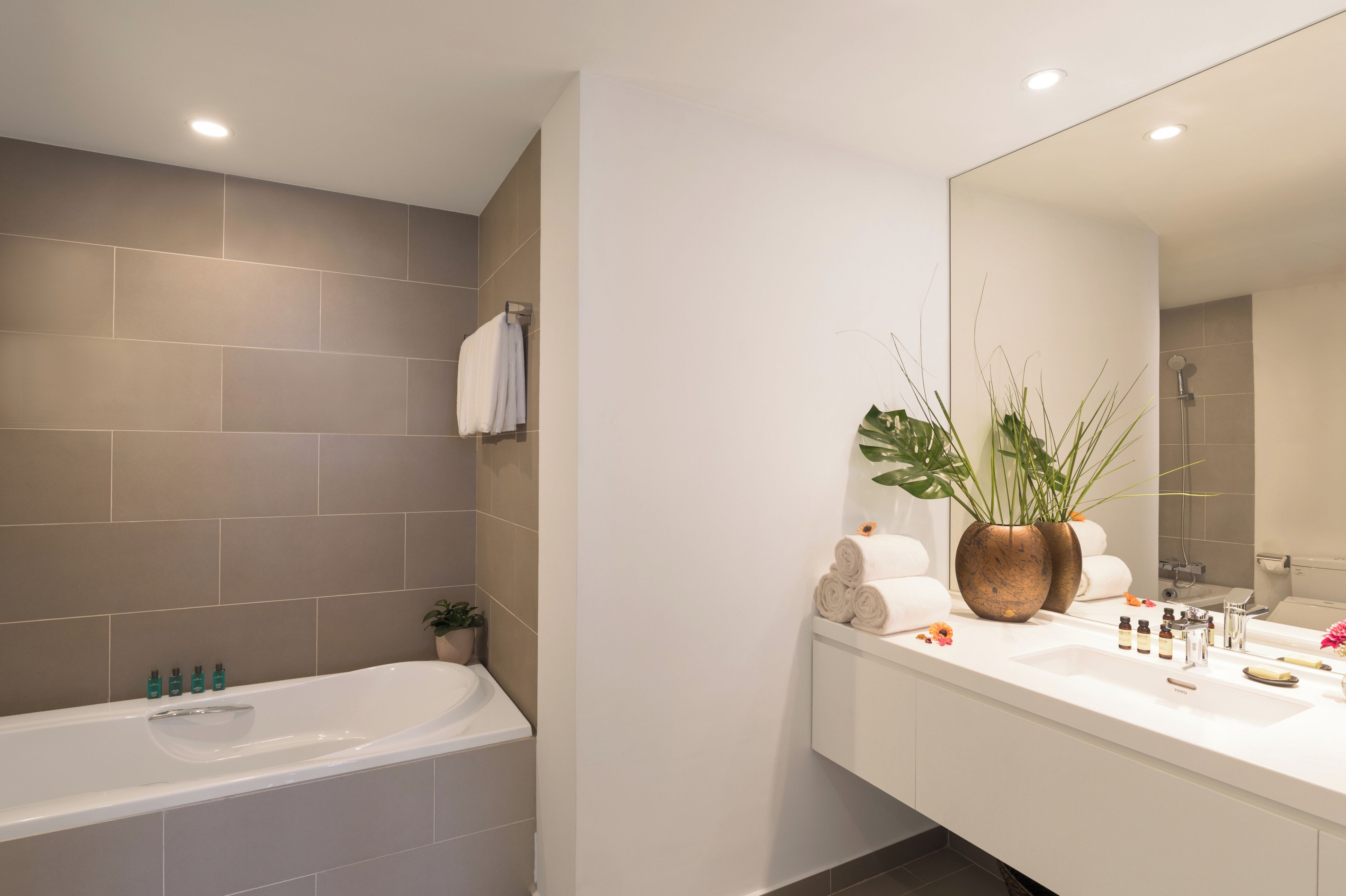Een moderne badkamer met een bad, een grote spiegel en een wastafelgedeelte met toiletartikelen.