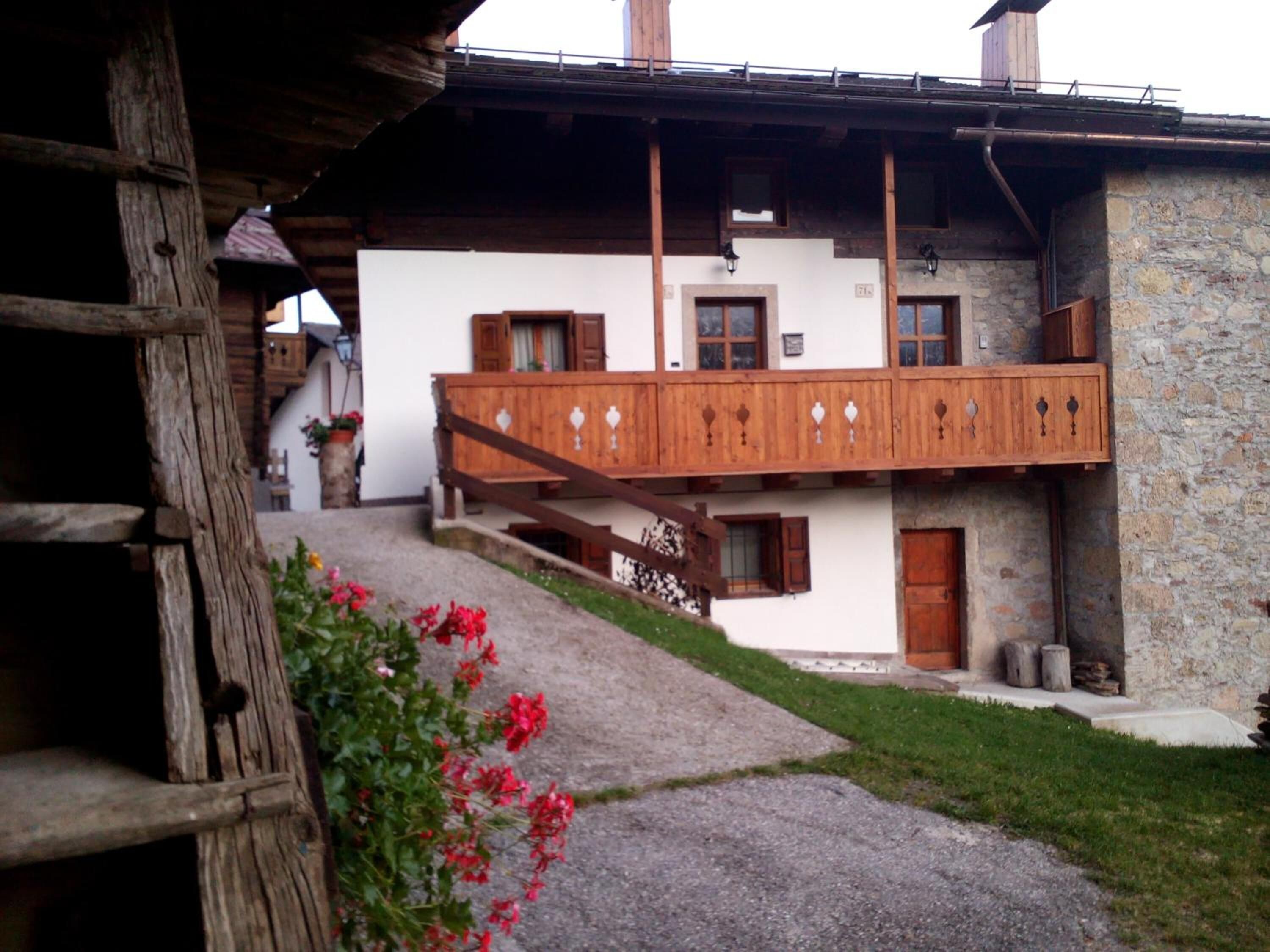 A traditional chalet with a wooden balcony, stone walls, and a gravel path leading to the entrance.