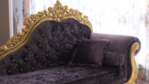A dark purple velvet sofa with gold ornate detailing and a tufted backrest, positioned in a room with floral curtains. - Love Paris (Hualien City)