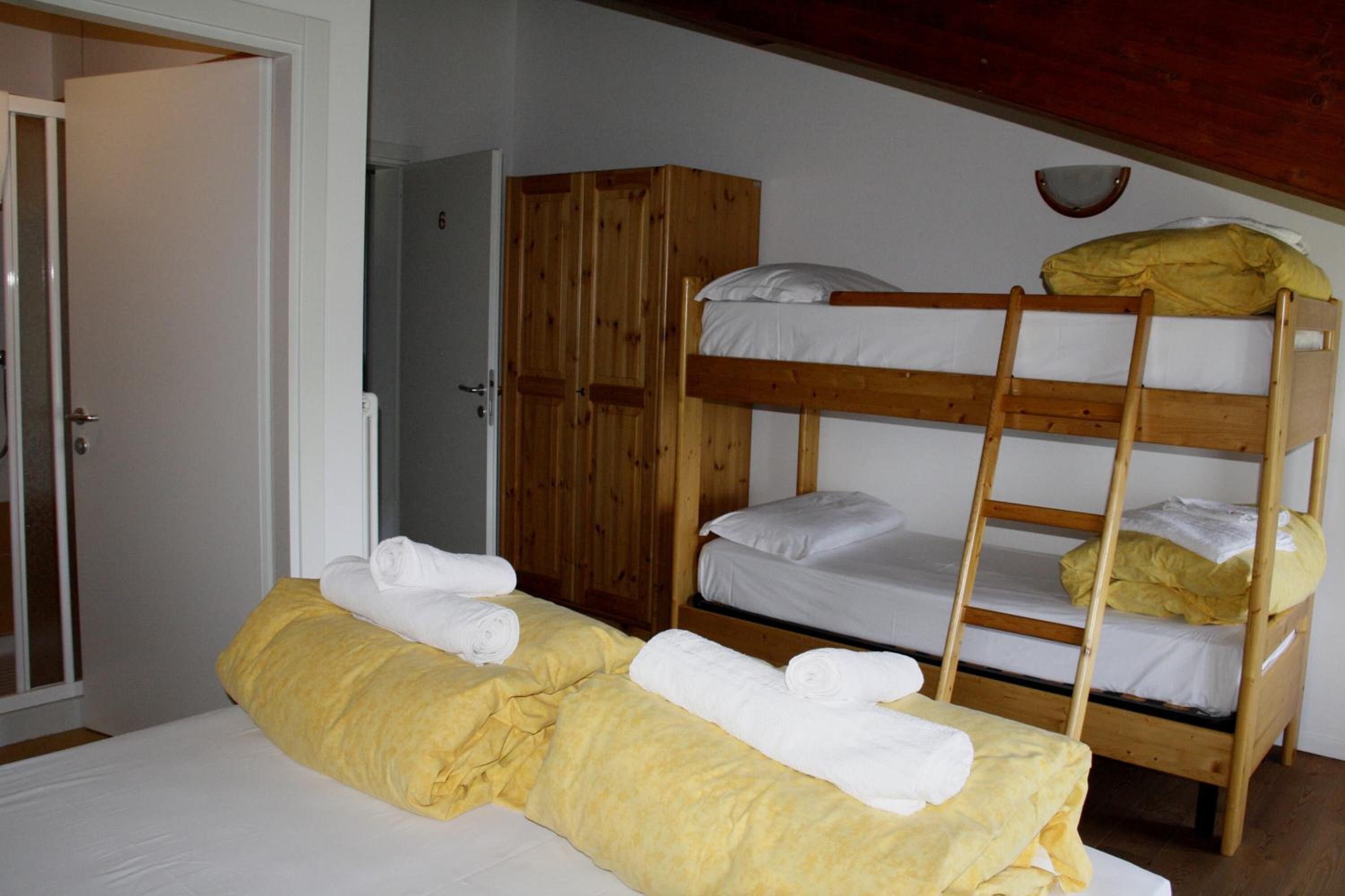 Ein Etagenbett mit weißer Bettwäsche und einer Holzleiter. Auf der unteren Etage liegt ein gelbes Handtuch, auf der oberen ein weißes. Im Hintergrund ist ein Holzschrank zu sehen.