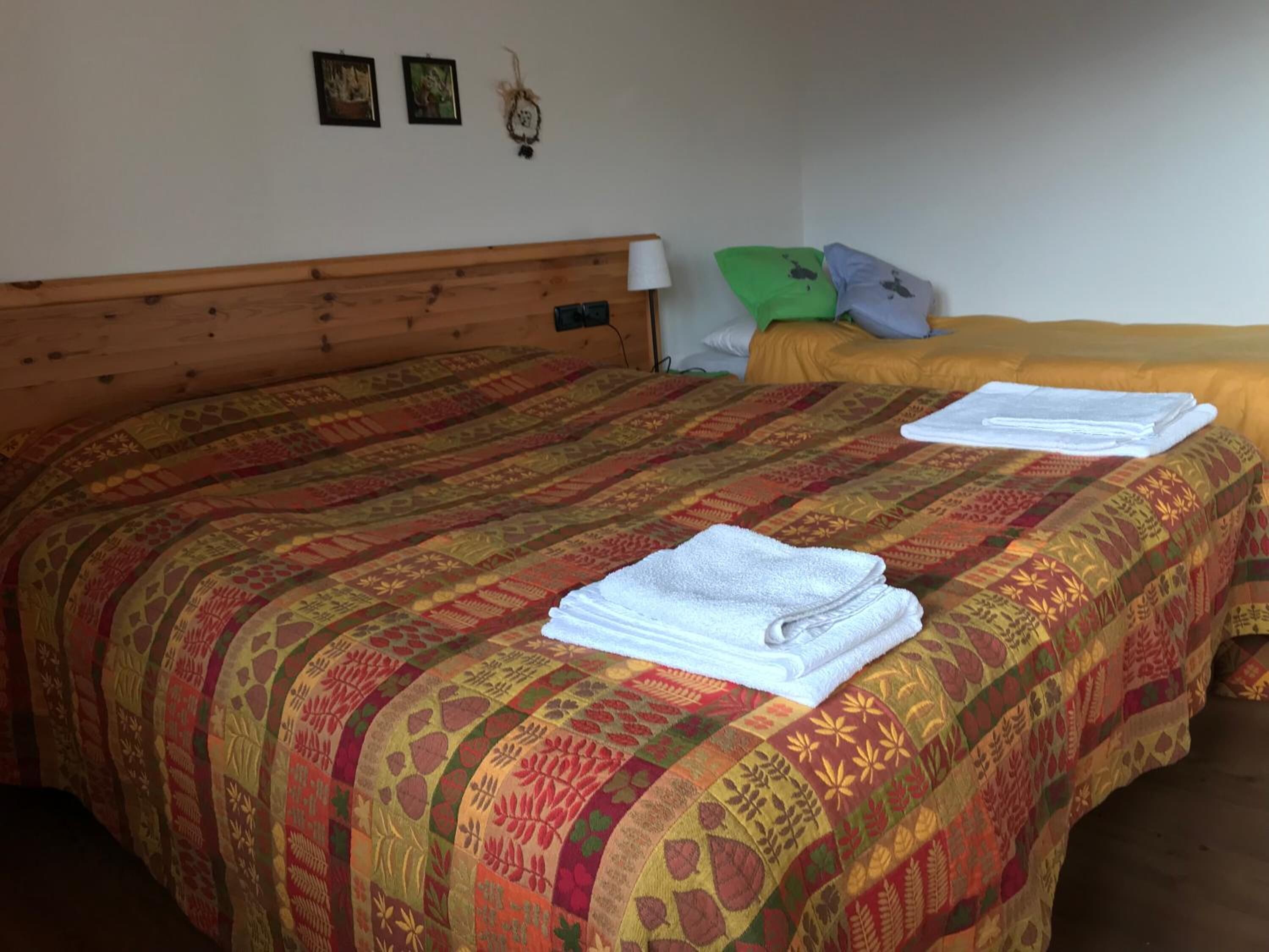 A room with two beds, each with a patterned bedspread and a stack of white towels on the bed.