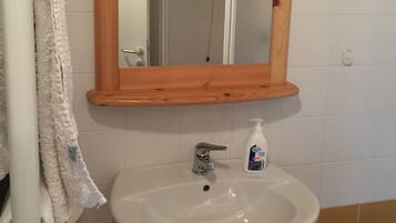 A bathroom with a wooden-framed mirror, a white sink, and a bottle of hand soap.