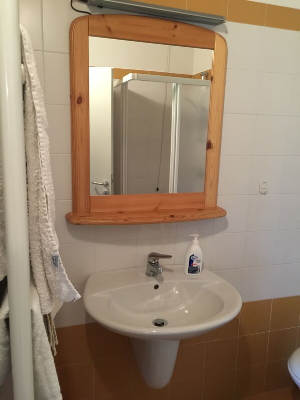 Une salle de bain avec un miroir encadré en bois, un lavabo blanc et un flacon de savon pour les mains.