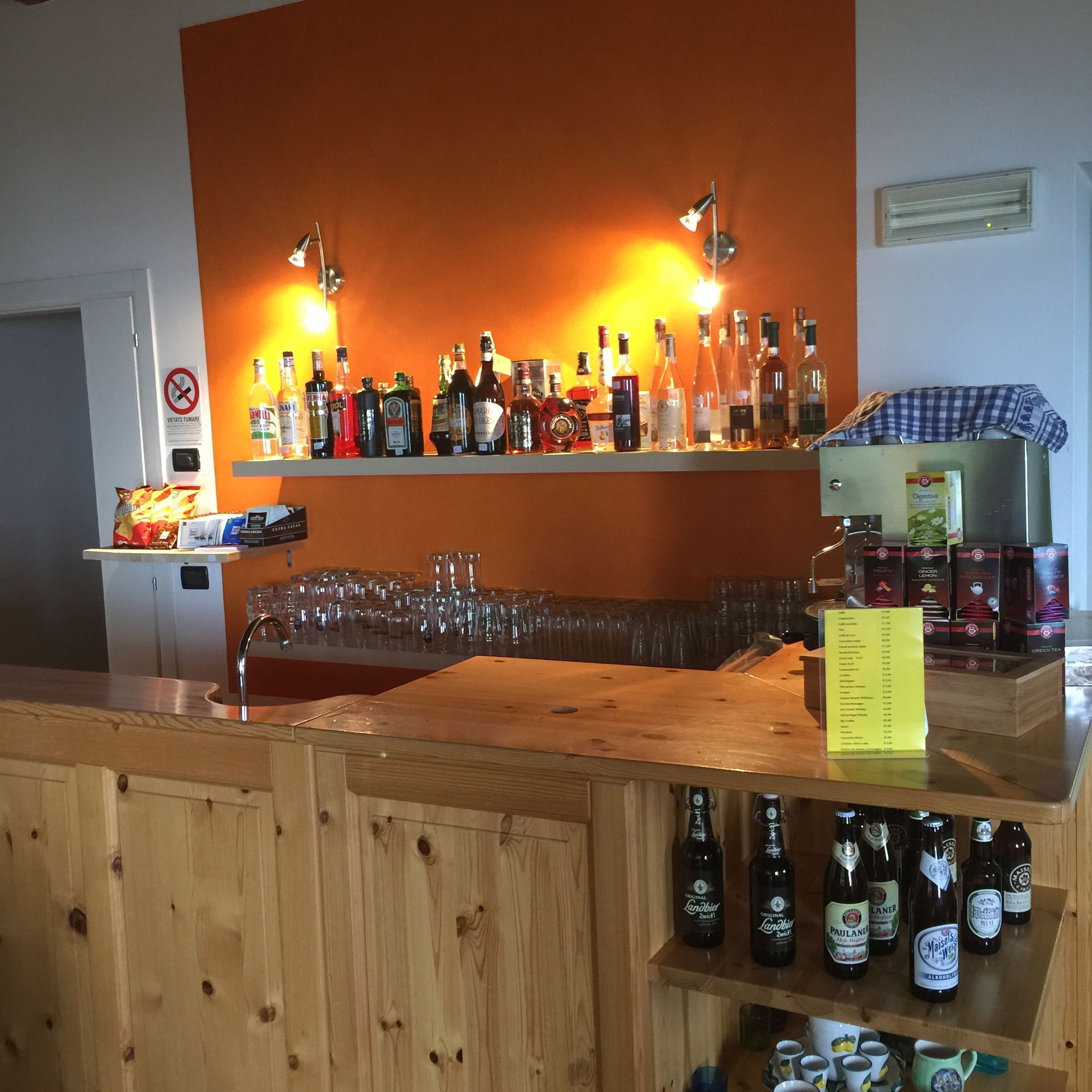 Un espace bar avec des étagères remplies de bouteilles d’alcool, de verres et un menu posé sur un comptoir en bois.