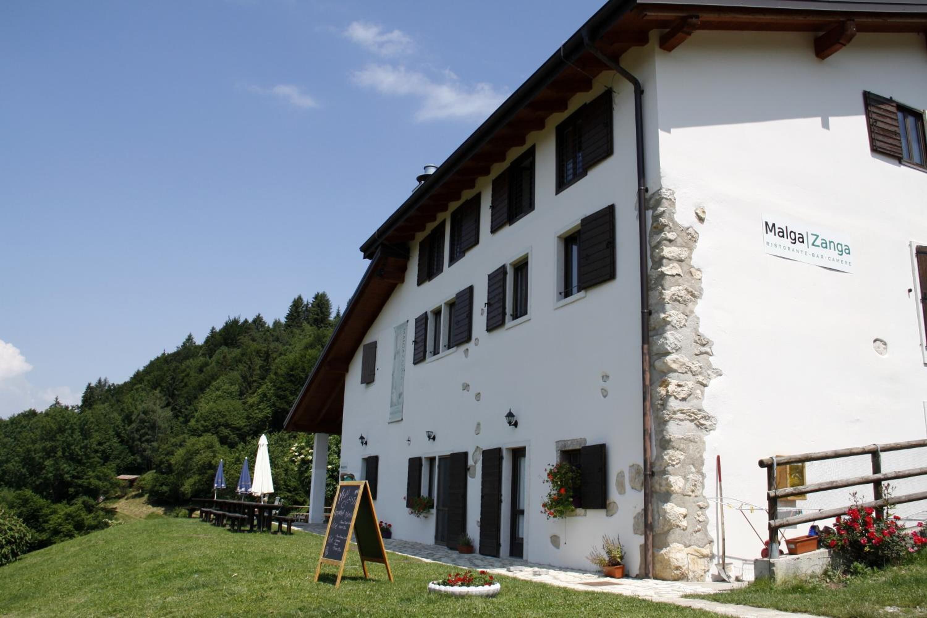 Un bâtiment à deux étages, sur lequel on peut lire l’inscription « Malga Zanga », et un mur en pierre.