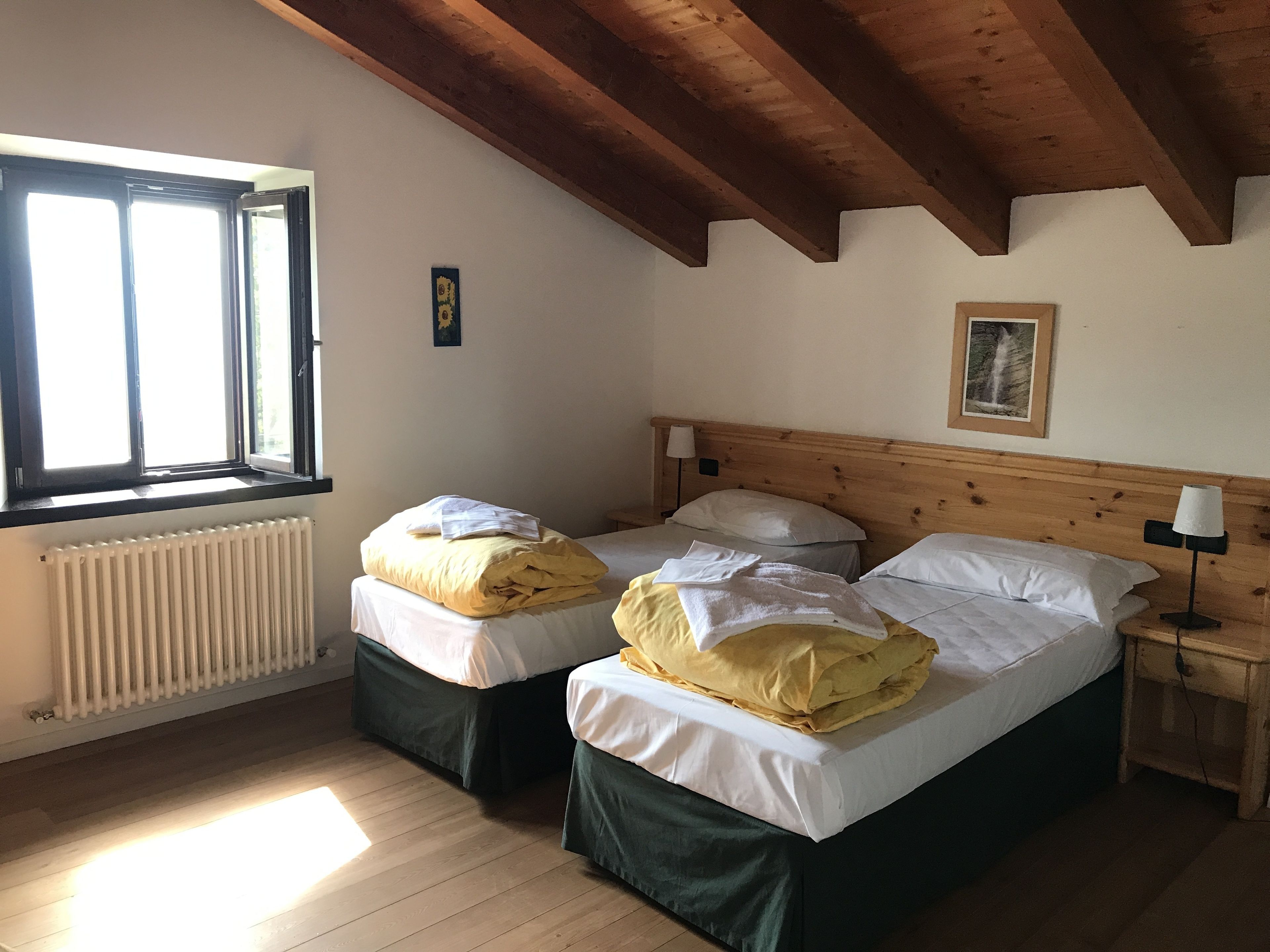 A room with two beds, a window, a radiator, and a wooden ceiling.